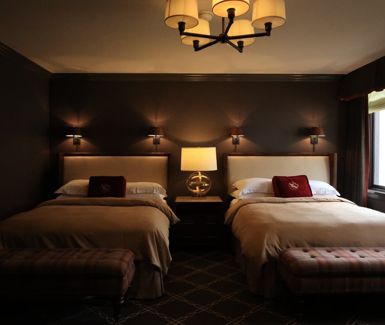 A hotel room with two beds, a chandelier, and a window