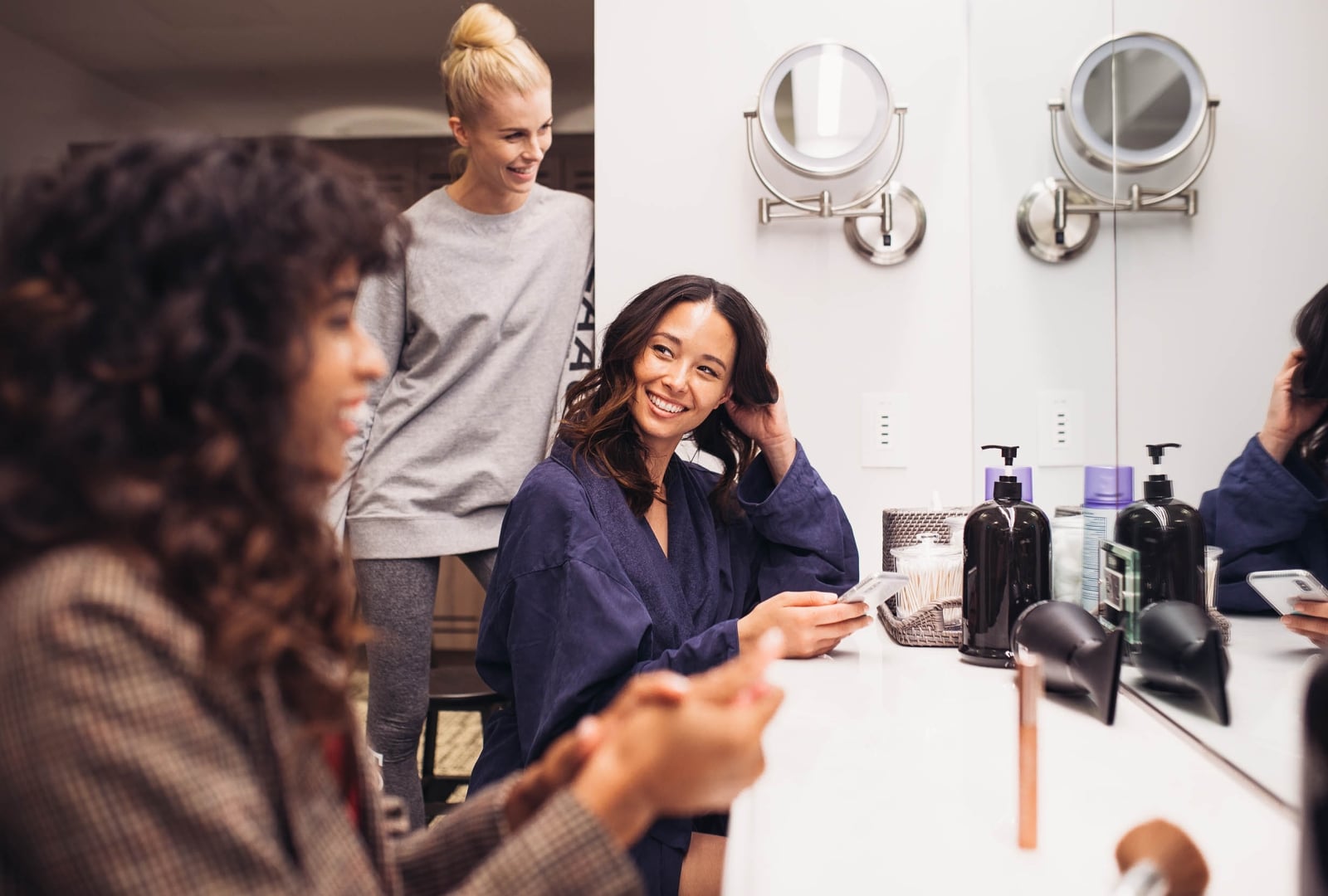 Several women in a locker room with a counter and mirrors