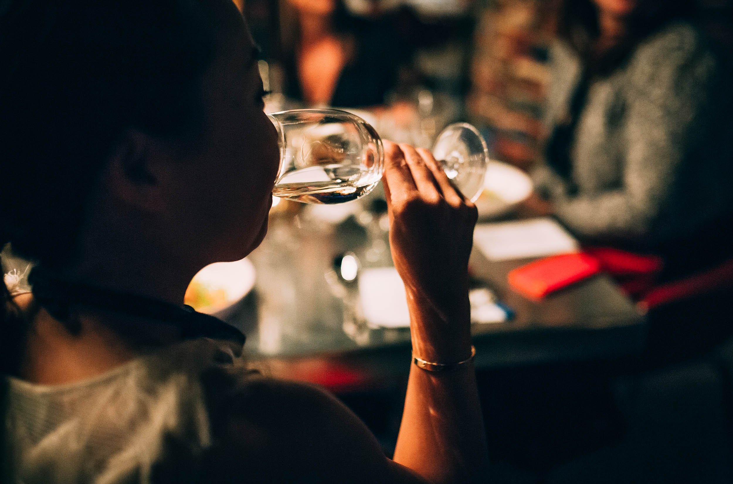 Person drinking wine at a table with group of friends