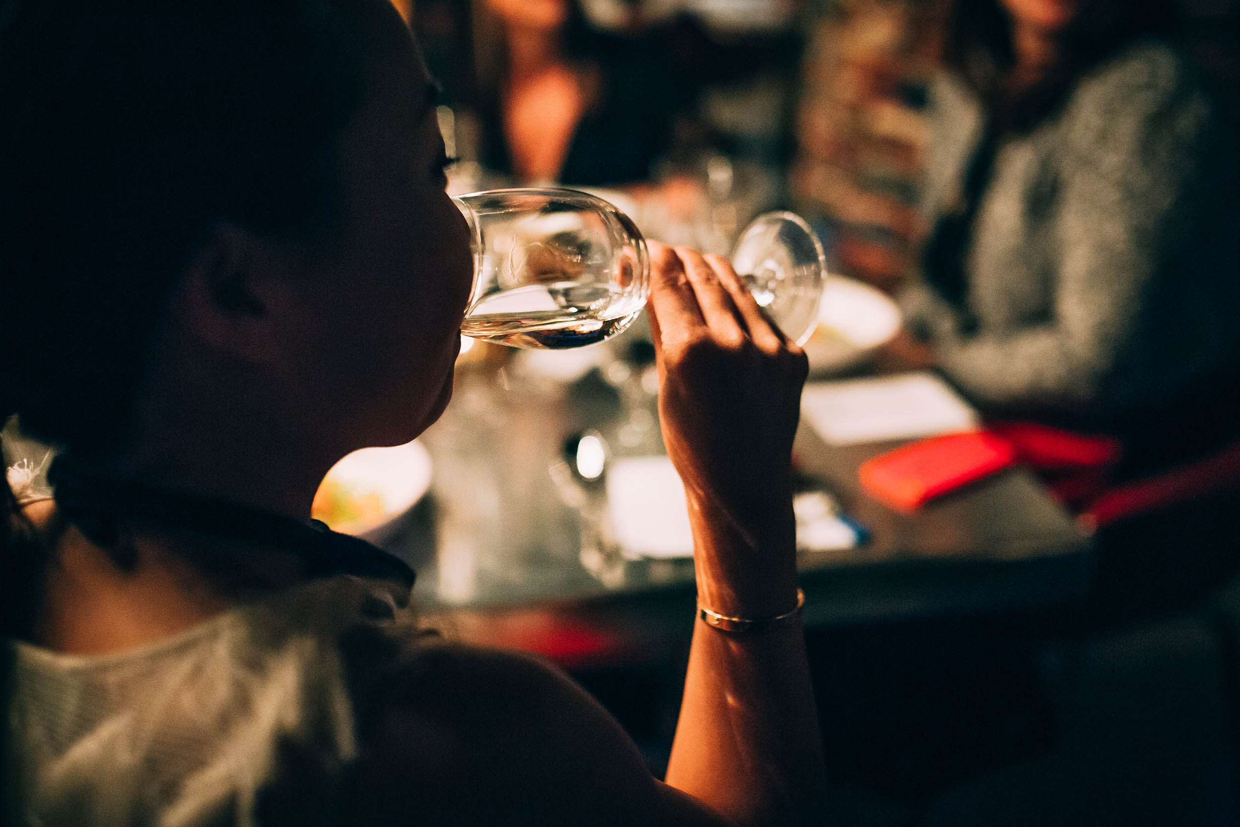 Person drinking wine at a table with group of friends