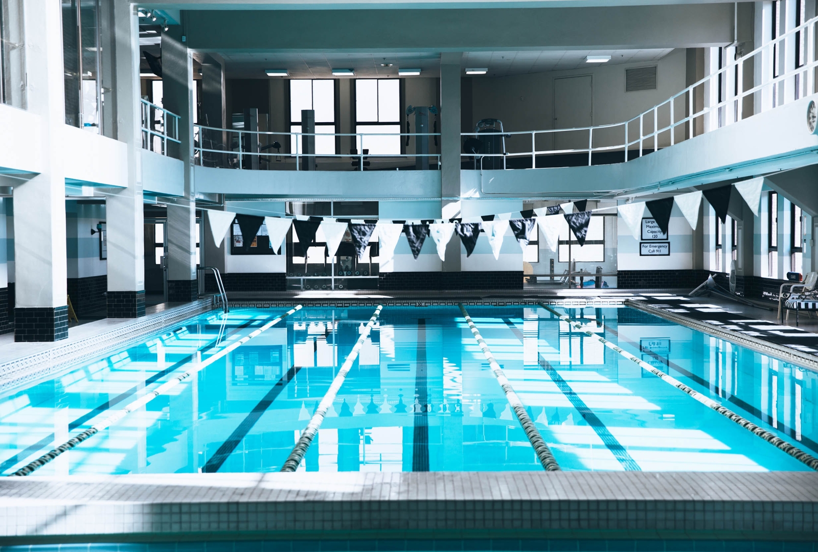 A large indoor lap pool with a balcony and flags hanging above it.