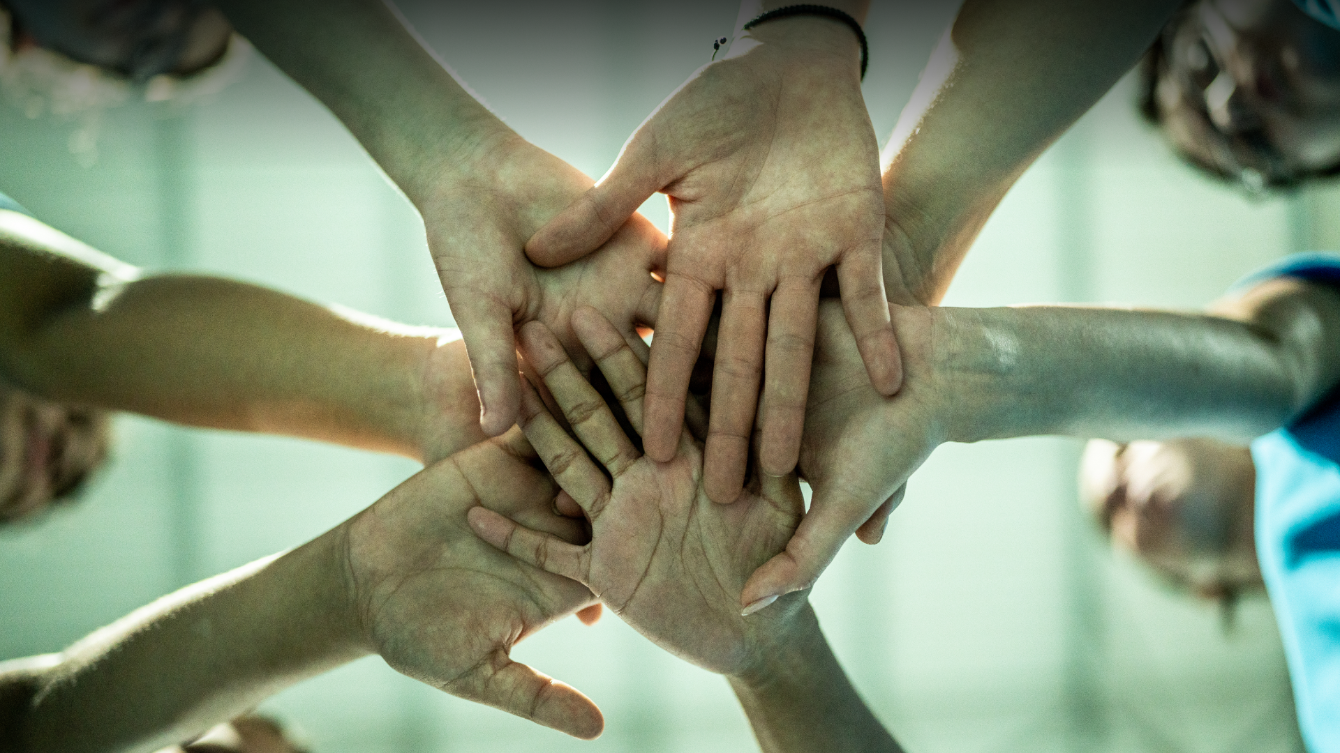 A diverse group of individuals standing in a circle, joining their hands together in unity and solidarity.