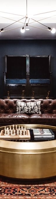 A luxurious lobby lounge with a brown leather sofa, a round gold coffee table, and a modern chandelier.
