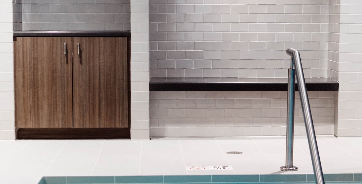 a small section of indoor pool with a metal handrail and a wooden cabinet against a white brick wall