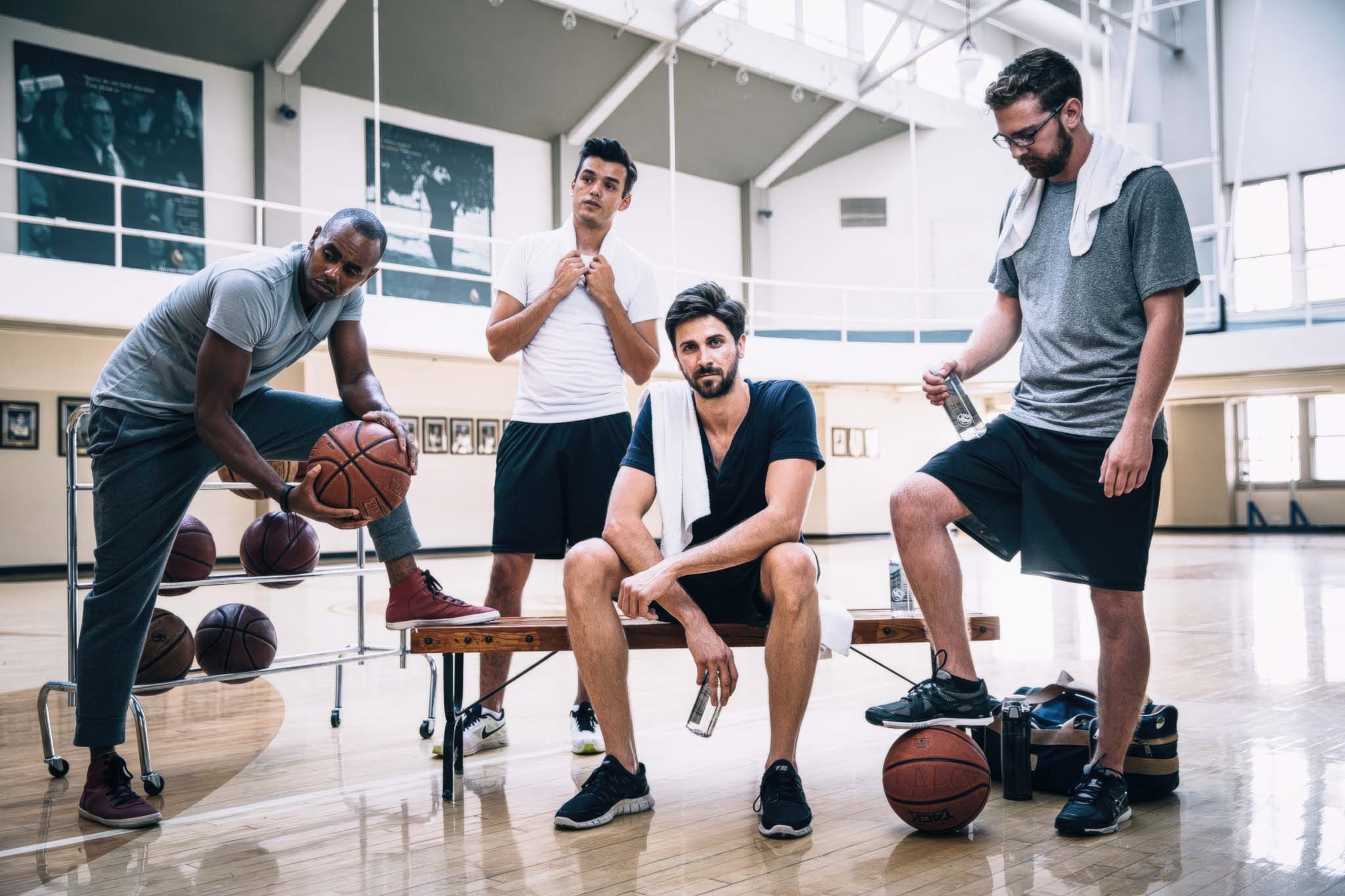 A group of men in athletic gear pose on a bench with basketballs