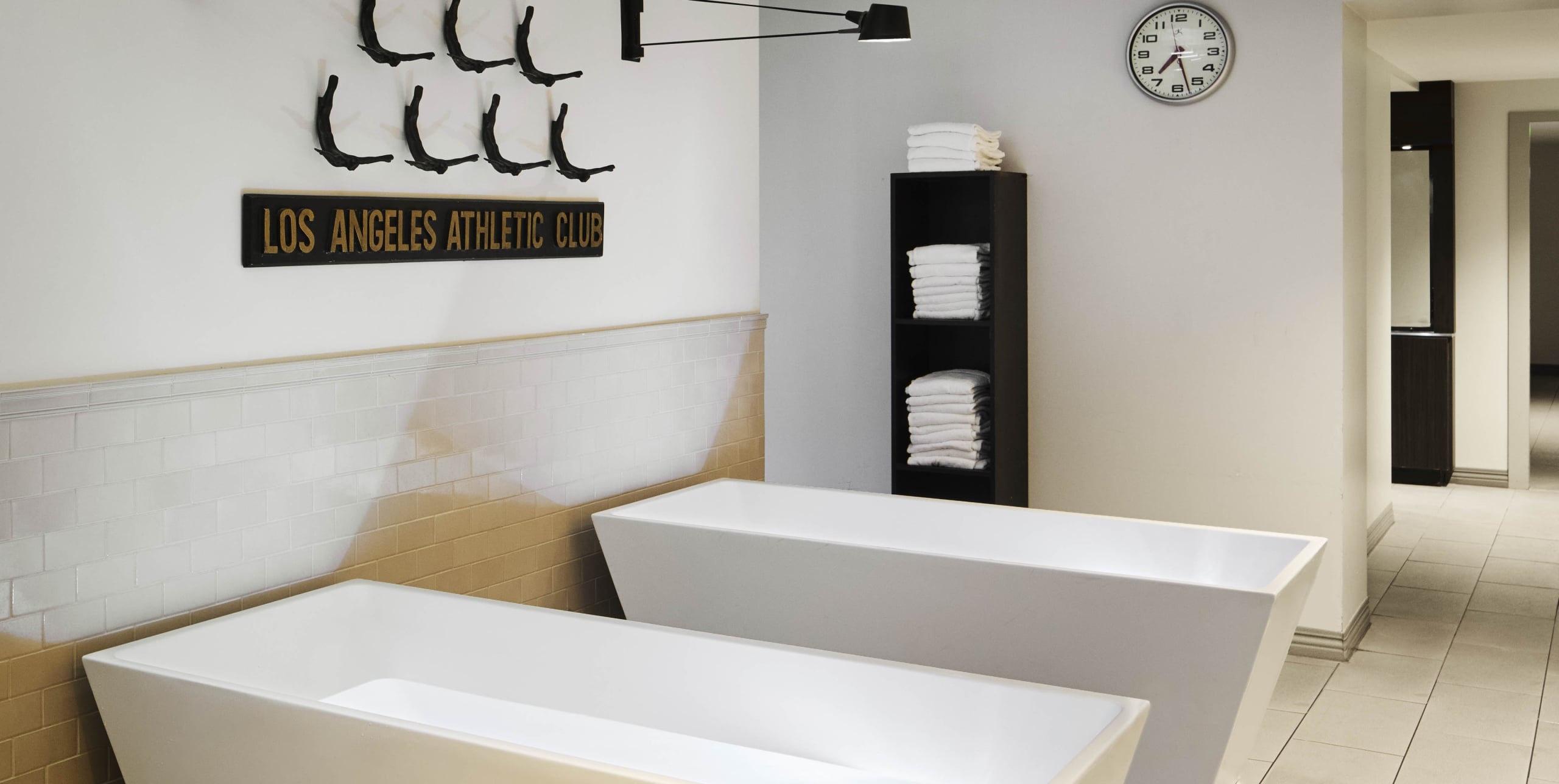 A serene spa area with two white tubs, a shelf with towels, and a clock on the wall.
