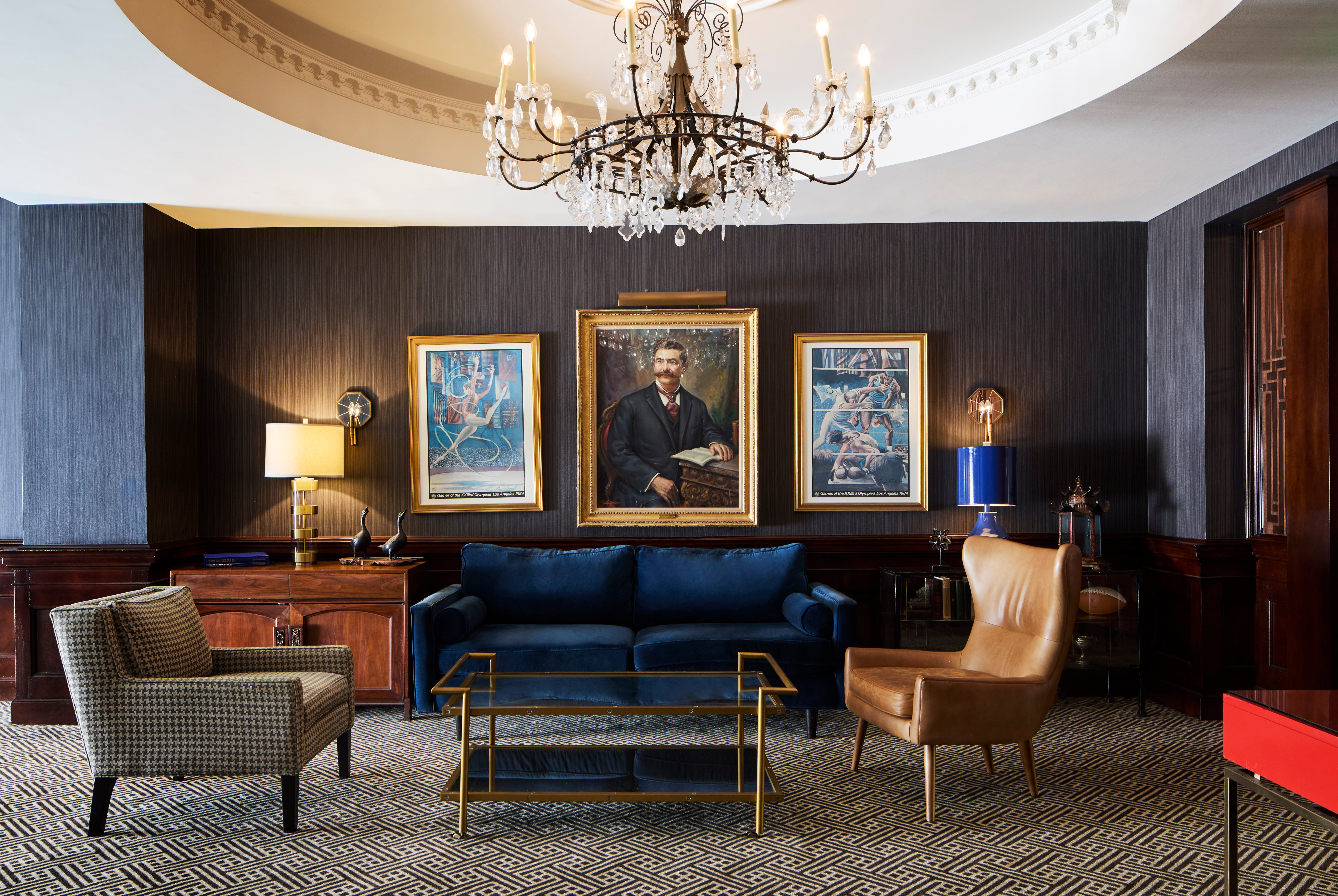 A luxurious lobby with a chandelier, sofa, armchair, coffee table, and paintings on the wall.
