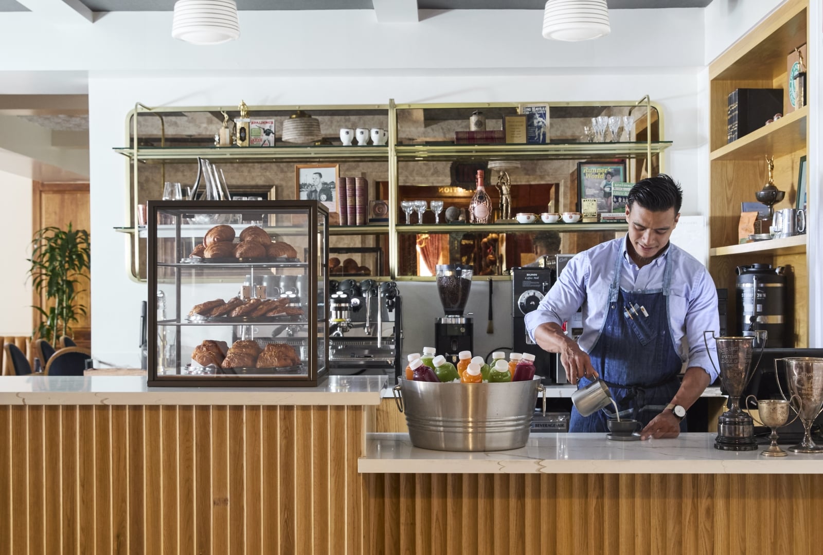 A barista prepares coffee at a counter with pastries and juice bottles on display.