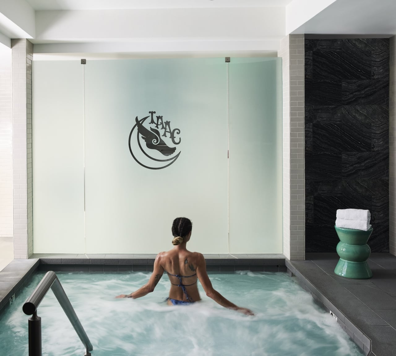 A woman relaxes in an indoor jacuzzi with bubbles and a tiled wall.