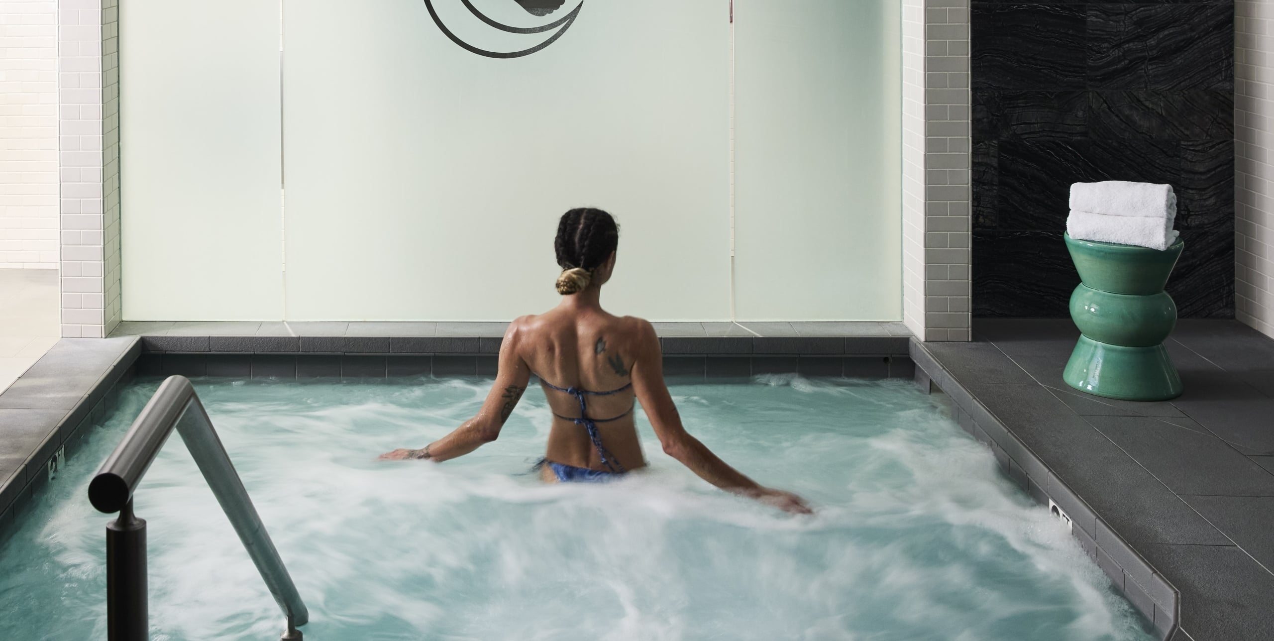 A woman relaxes in a bubbling hot tub with towels nearby.