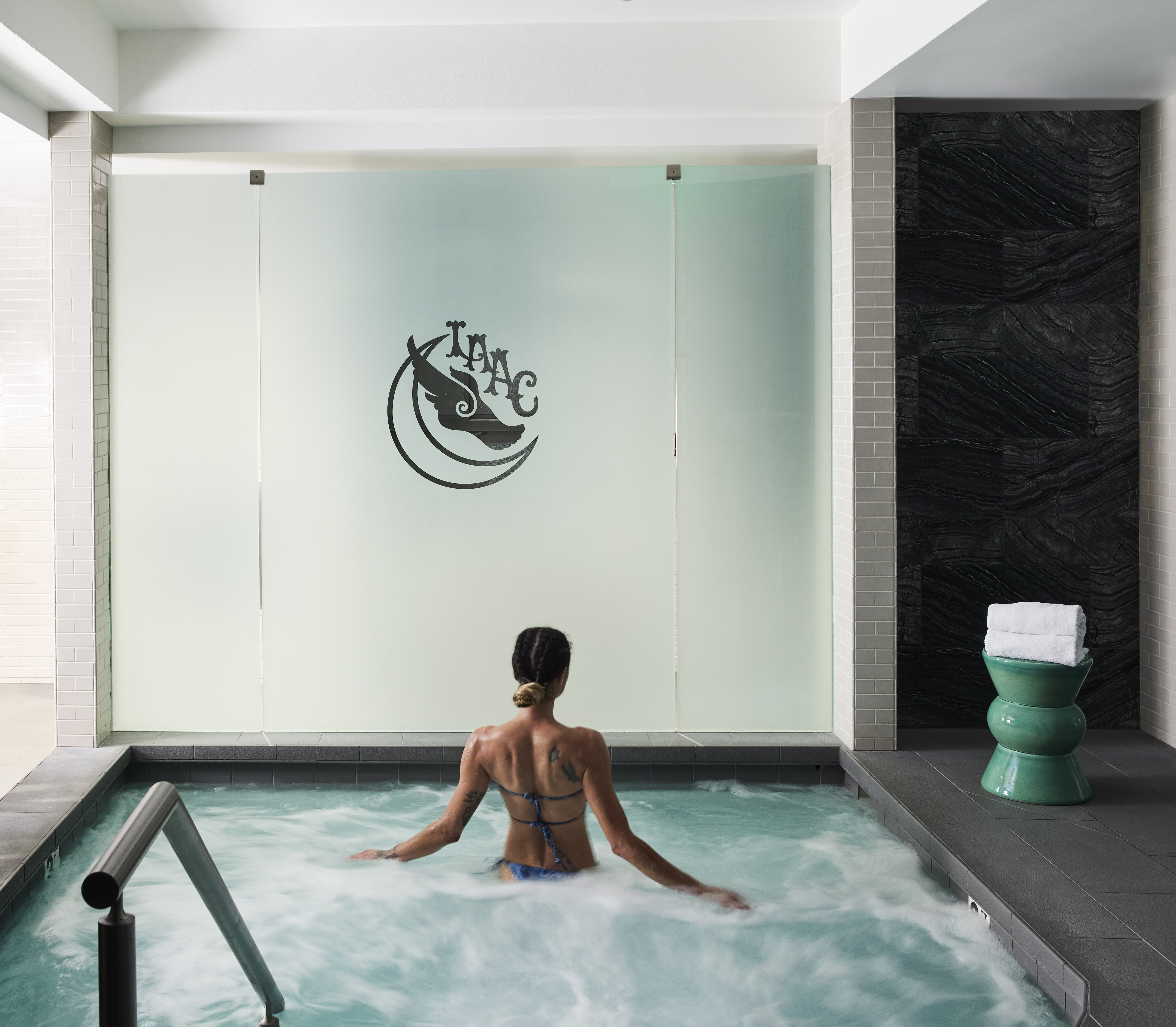 A woman relaxes in an indoor jacuzzi with bubbles and a tiled wall.