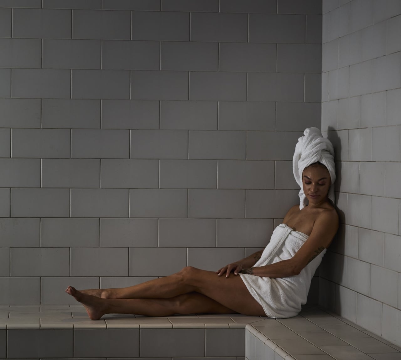 A woman in a towel sitting on a tiled bench in a spa area.