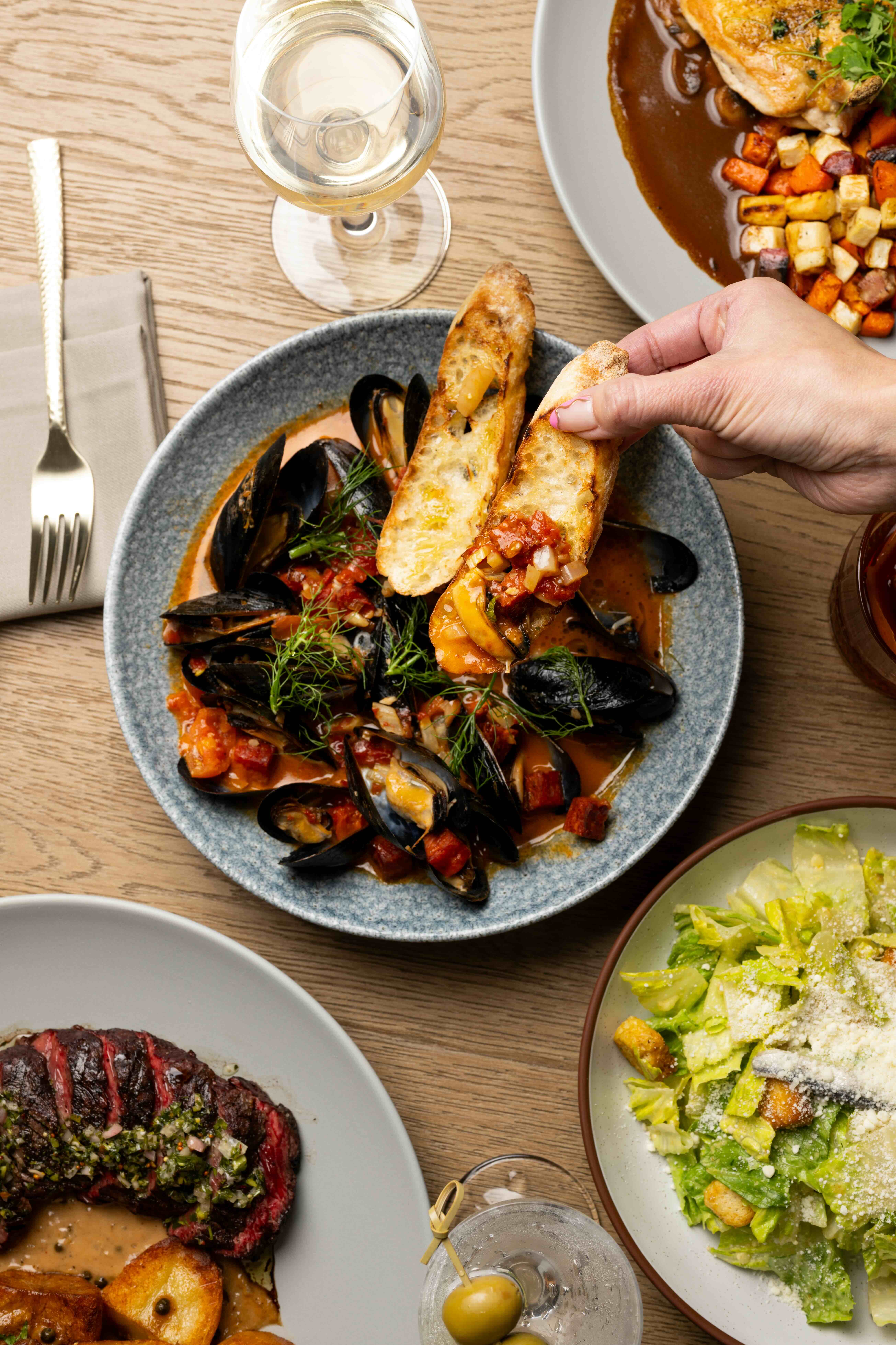 a hand dipping bread into a bowl of mussels