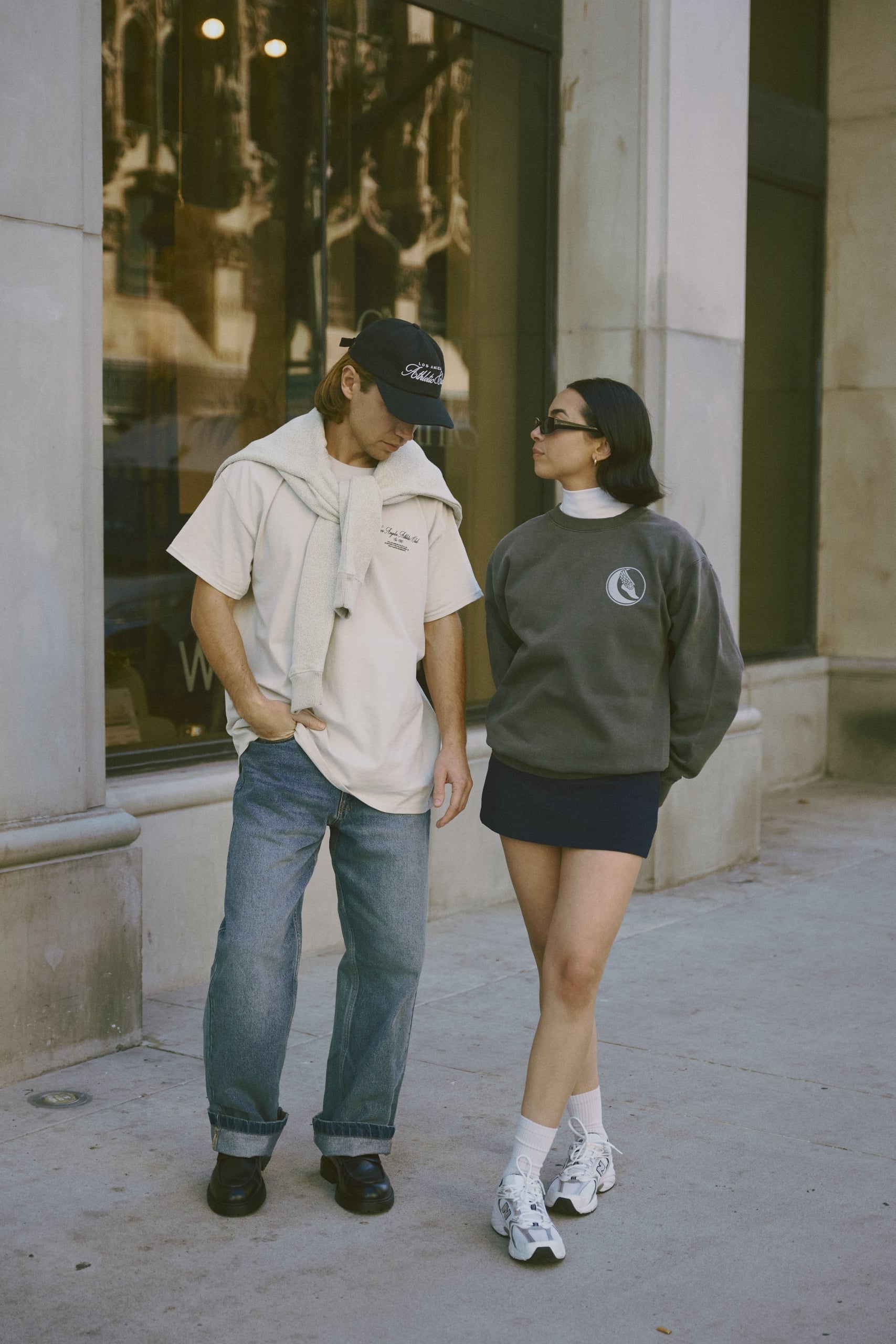 A man and woman wearing Los Angeles Athletics Club clothing poses on the street