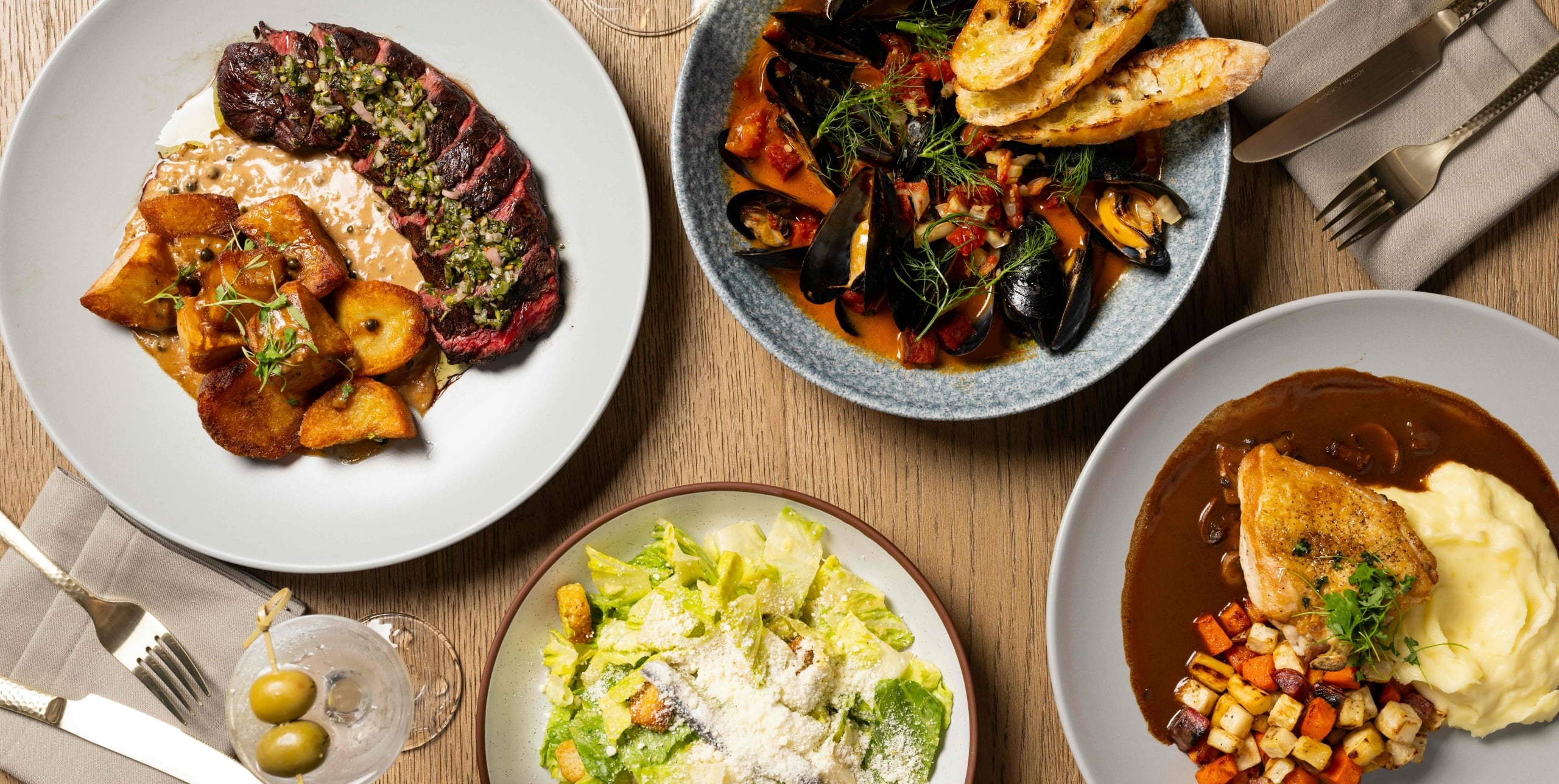A selection of dishes on a table, including steak, mussels, salad, and chicken.